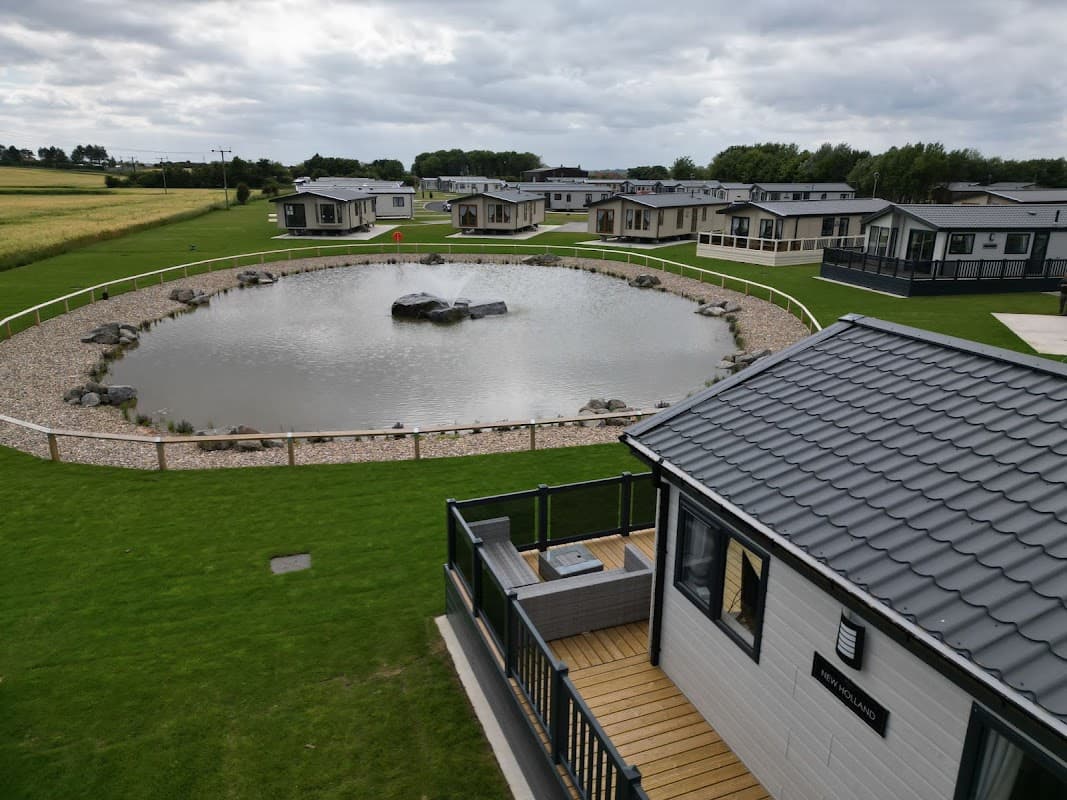 Hornsea Leisure Park features modern lodges around a landscaped pond with a central rock, set in a green, open area.