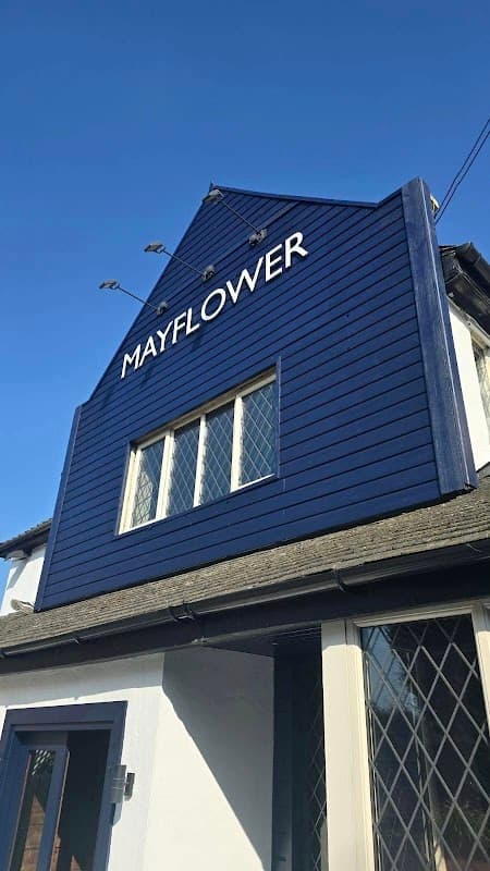 Blue wooden exterior of The Mayflower pub, featuring a prominent sign and diamond-patterned windows against a clear sky.