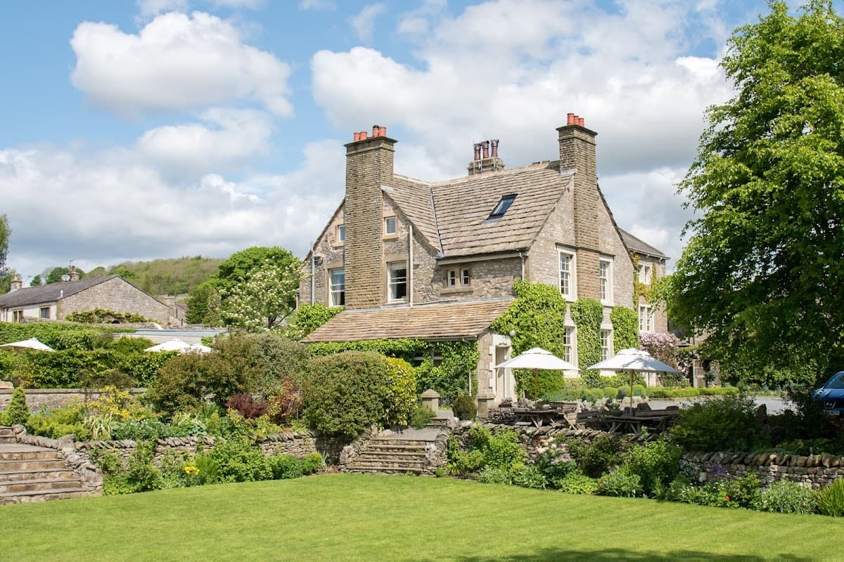 Historic stone venue surrounded by lush gardens and trees, with outdoor seating and a bright blue sky overhead.