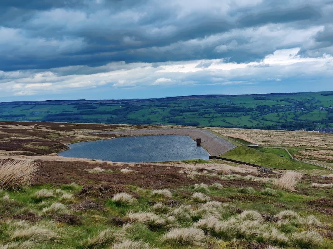 Baildon Moor landscape with a small pond, grassy moorland, and rolling hills under a cloudy sky.