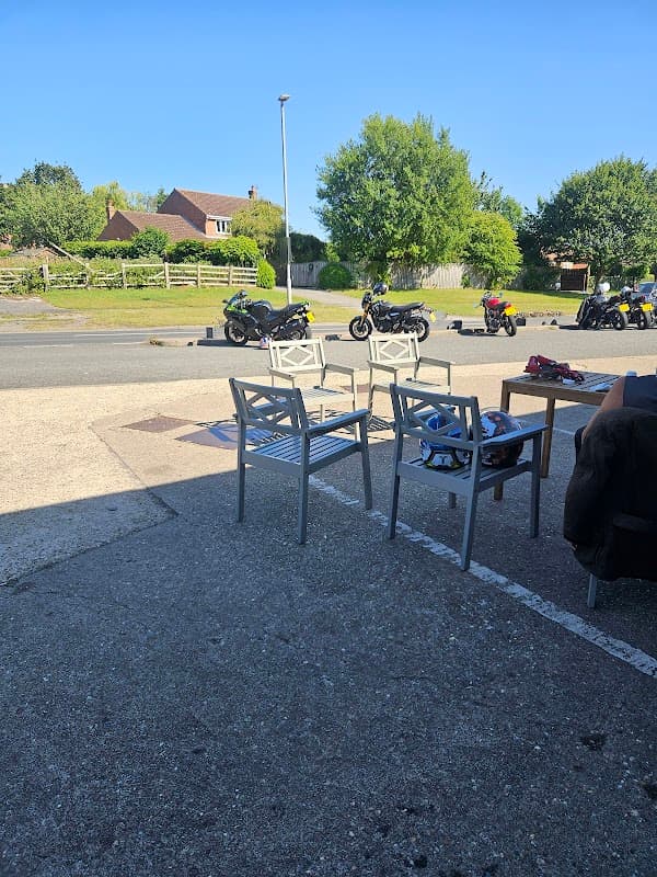 View from a grocer's patio with empty chairs, parked motorcycles, and greenery in the background under a clear blue sky.