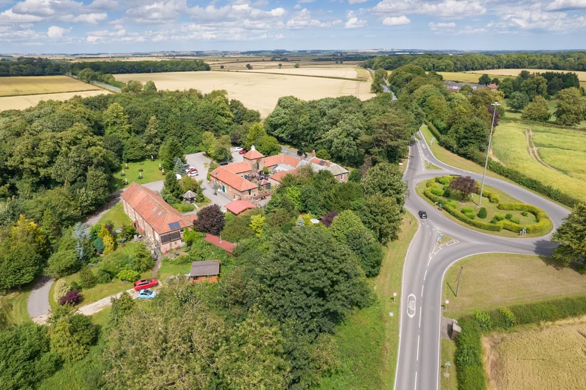 Aerial view of Wolds Village hotel surrounded by greenery, fields, and a circular road in Bainton, Yorkshire.