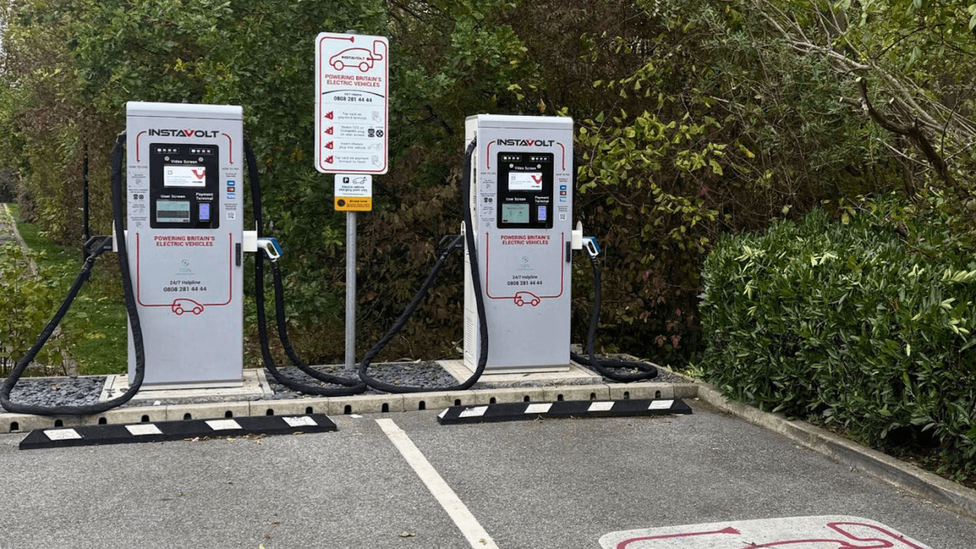 Two InstaVolt electric vehicle charging stations with digital displays and charging cables, located in a parking area.