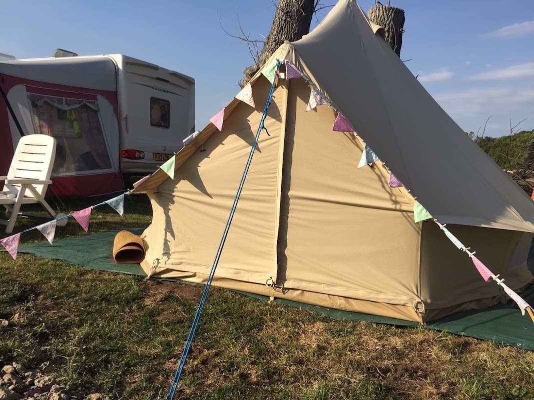 A beige tent with colorful bunting, a white chair, and a caravan in a grassy campsite under a clear blue sky.