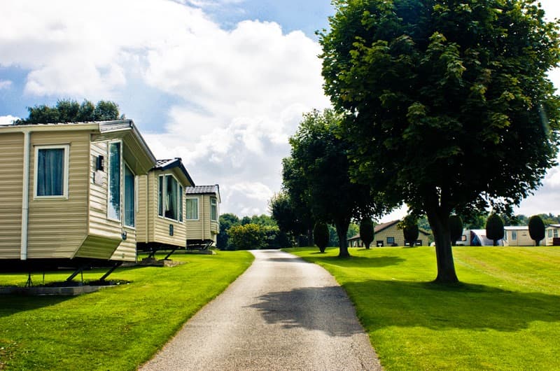 Caravan park with neatly arranged caravans along a tree-lined path and lush green lawns on a sunny day.