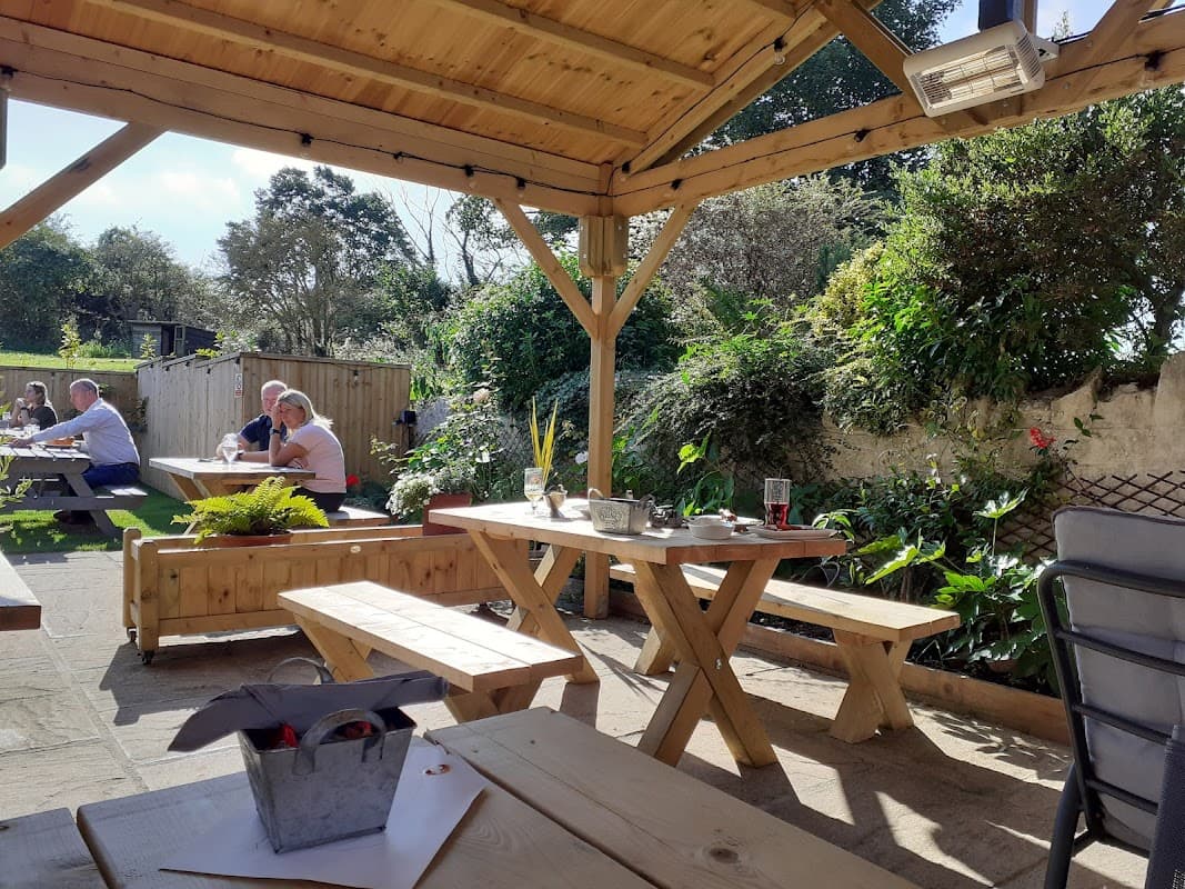 Outdoor seating area at The Crooked Billet Inn, featuring wooden tables, plants, and patrons enjoying the sunny day.