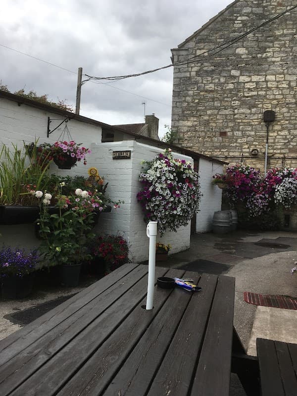 A rustic outdoor bar area with wooden tables, vibrant flower baskets, and a stone building in the background.