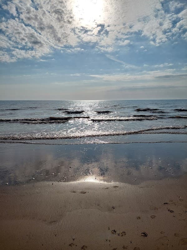 Sunlight reflects on calm waves at Barmston Beach, with a clear blue sky and scattered clouds above.
