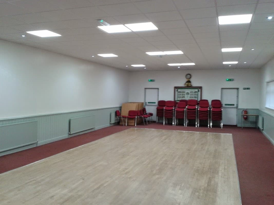 Spacious community hall with wooden floor, stacked red chairs, and bright lighting.