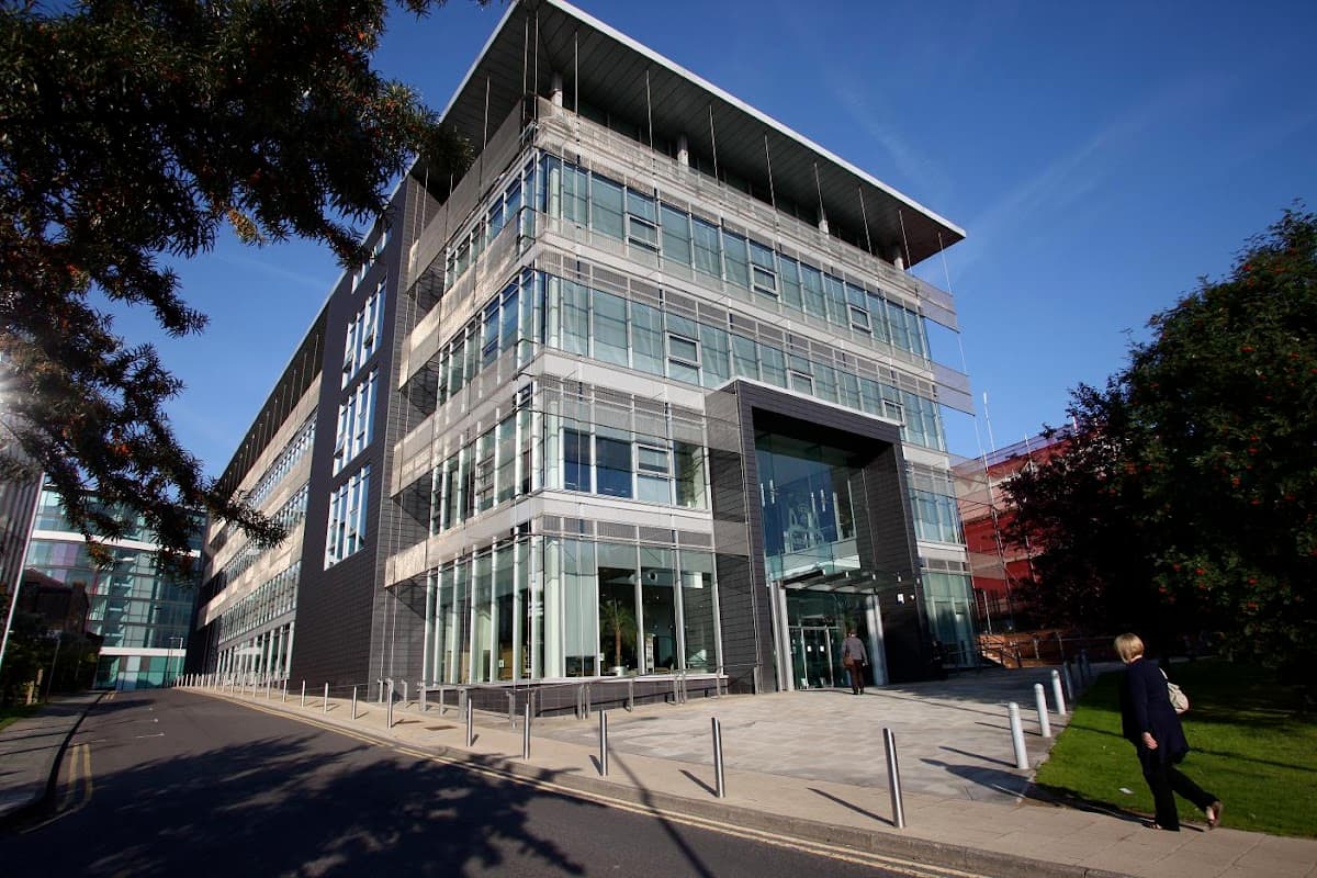 Modern glass-fronted building with a sleek design, surrounded by greenery and a clear blue sky.