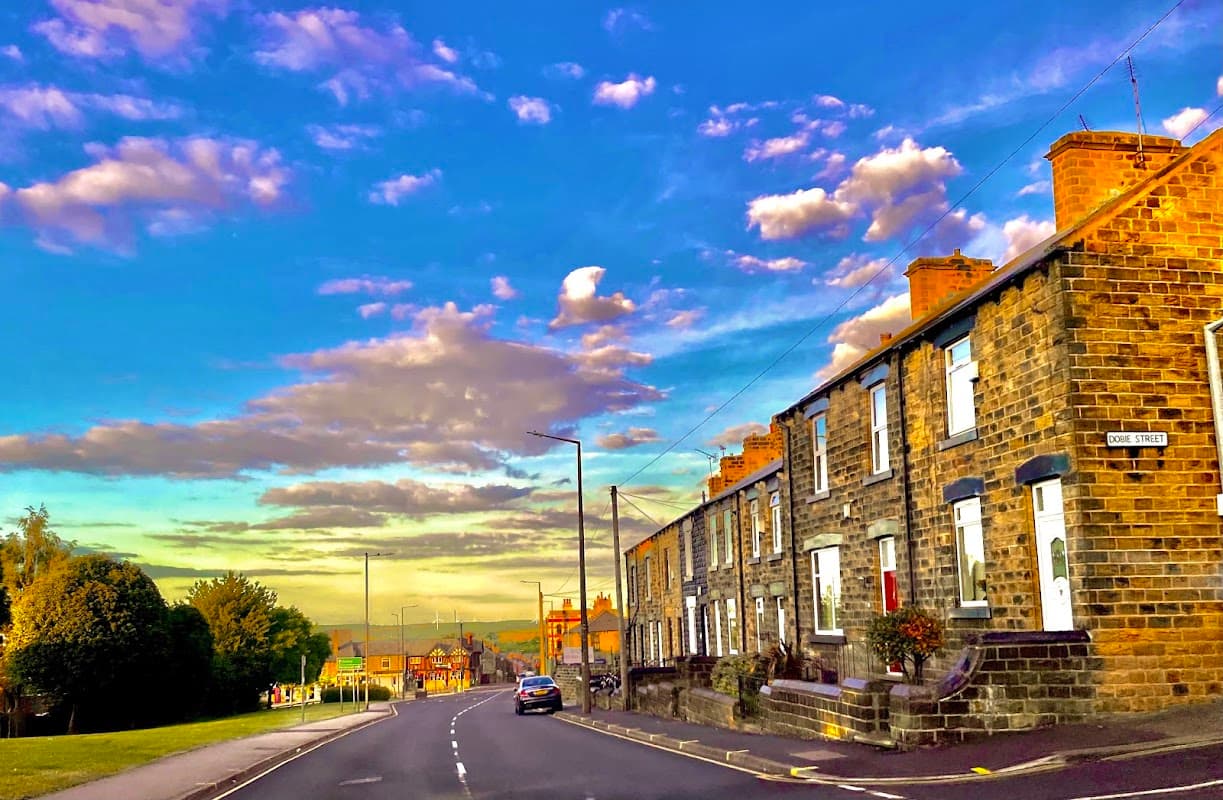 Burleigh Street West Commuter Car Park with stone houses, lush greenery, and a vibrant sky filled with clouds.