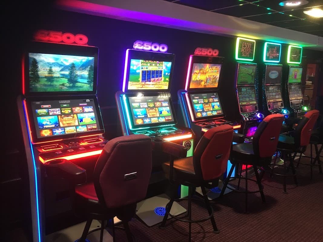 Brightly lit slot machines with colorful screens and chairs in a gaming area at Buzz Bingo, Barnsley.