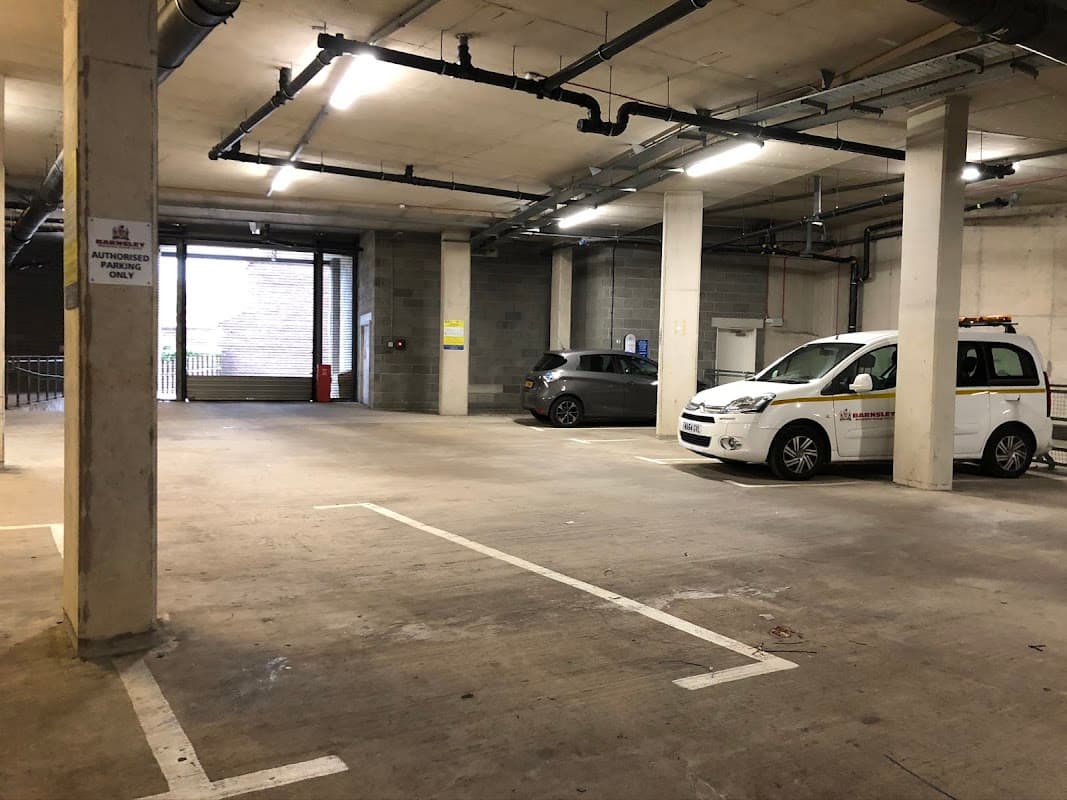 Electric vehicle charging station in a parking garage with two parked cars and visible signage.