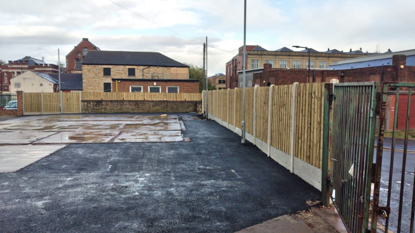 Pay & Display car park with wooden fencing, asphalt surface, and nearby buildings under a cloudy sky in Barnsley.