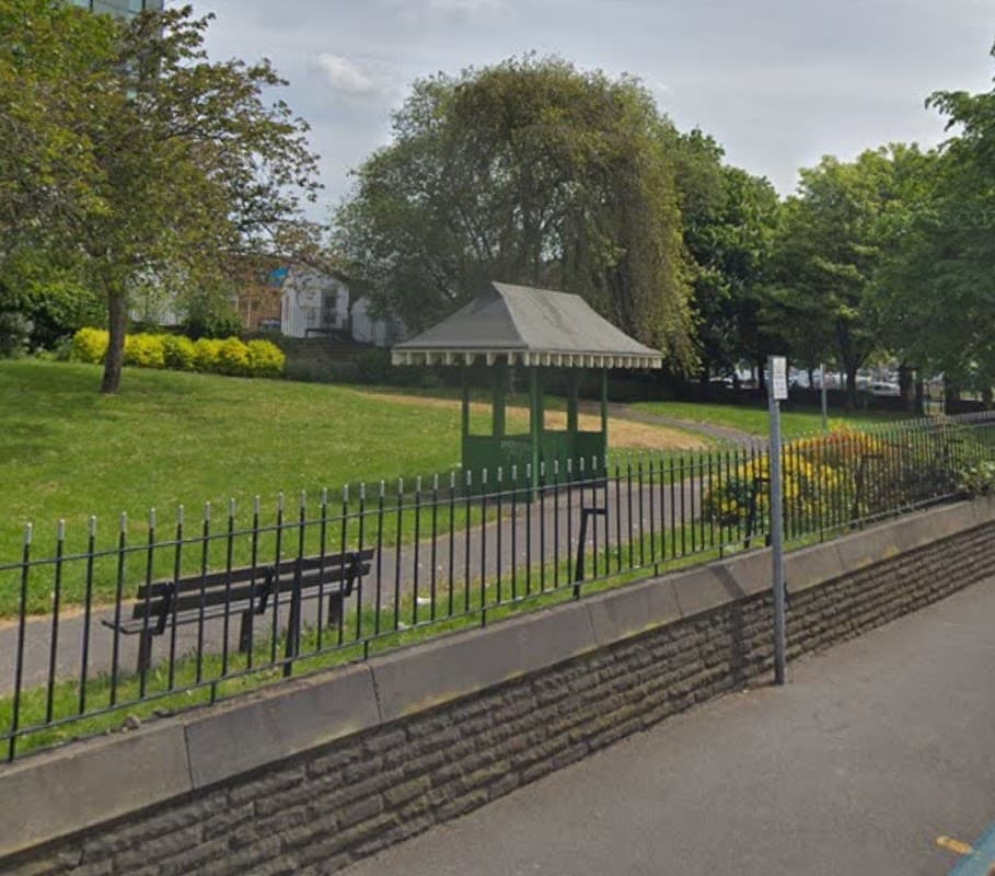 Green gazebo surrounded by trees and shrubs, with a path and benches in Sparrow Park, Barnsley.