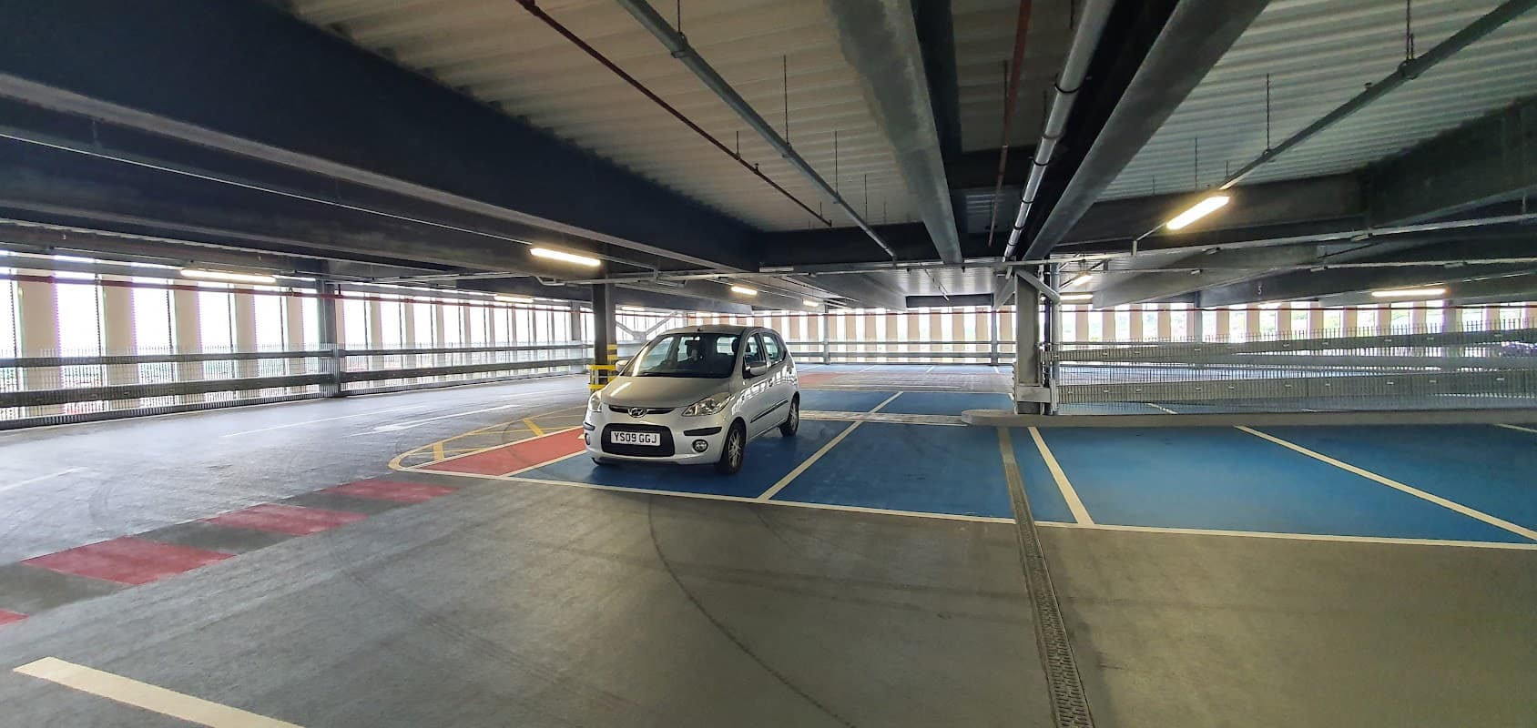 A spacious multi-level car park with a silver car parked in a blue bay and natural light streaming through windows.
