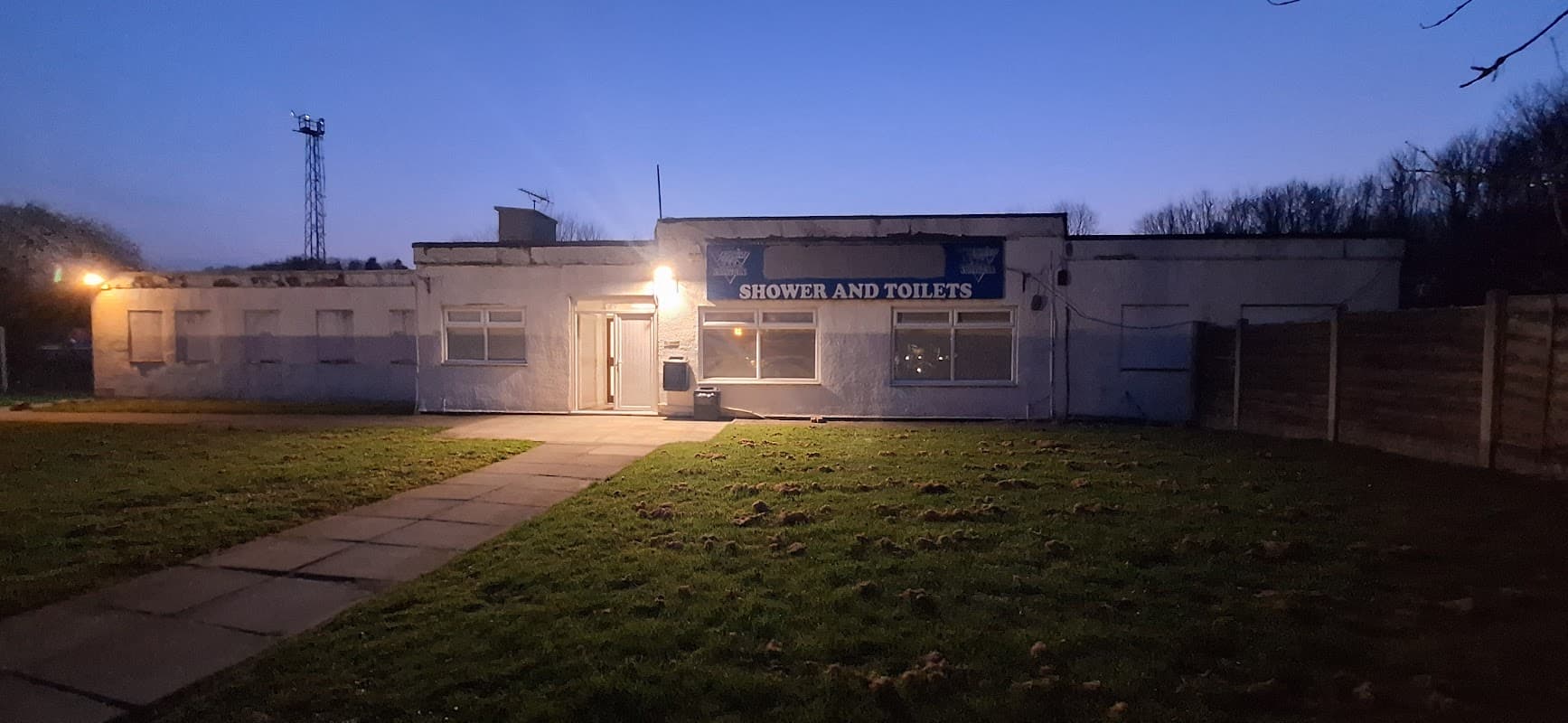 Cafe building with a sign reading "SHOWER AND TOILETS," surrounded by grass and trees at dusk.