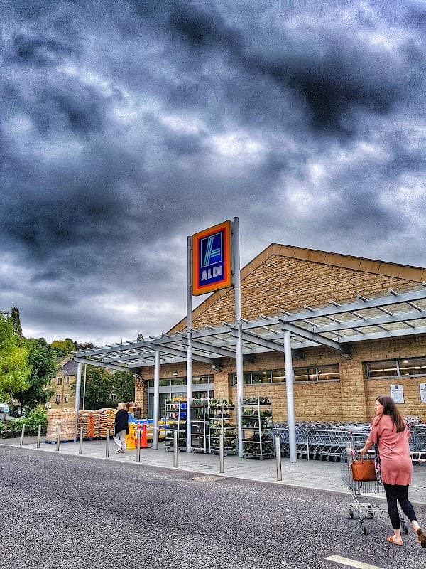 ALDI storefront in Batley, Yorkshire, with shoppers and a cloudy sky overhead.