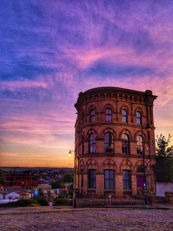 Historic stone building with rounded edges against a vibrant sunset sky in Batley, Yorkshire.