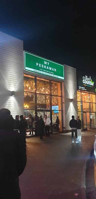 My Peshawar restaurant entrance at night, with people gathered outside and illuminated signage.