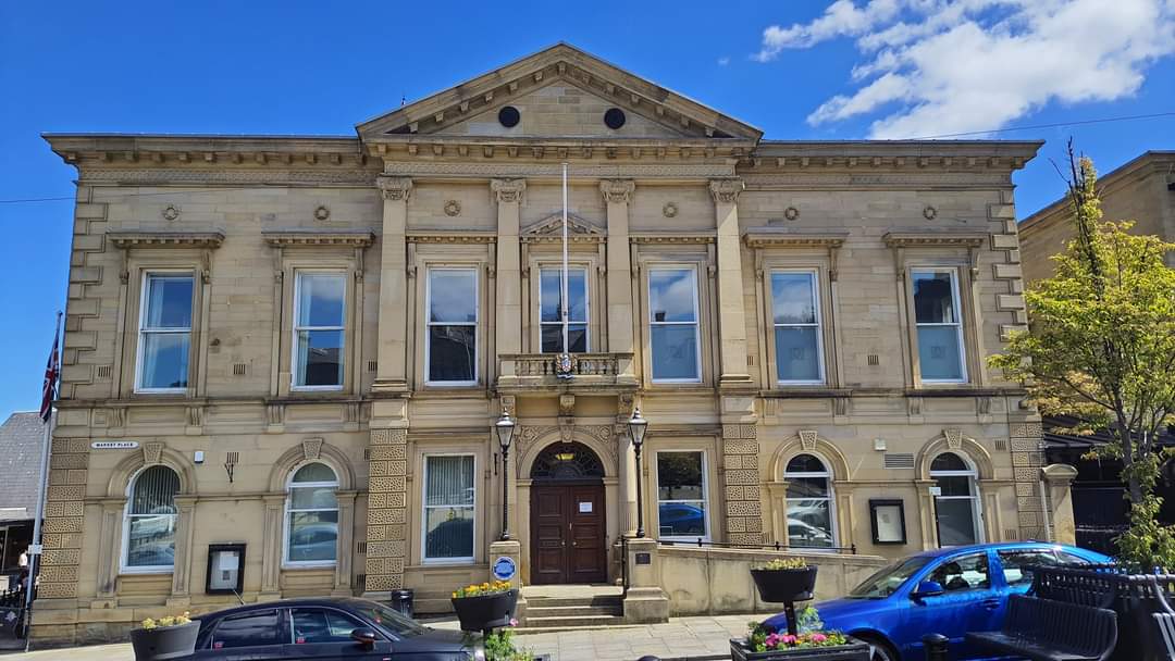 Historic Batley Town Hall with ornate stone facade, large windows, and decorative details under a blue sky.