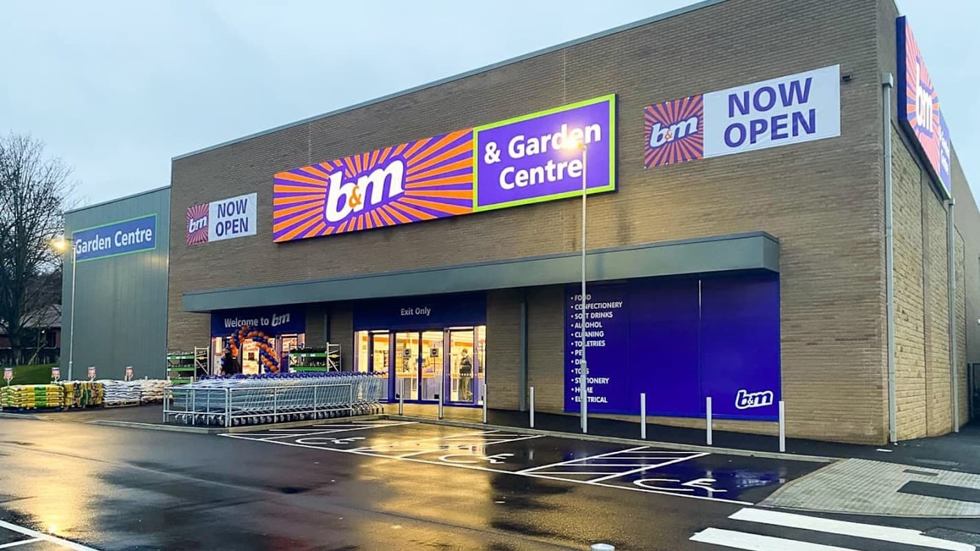 B&M store with bright signage, garden centre entrance, and shopping carts outside on a wet pavement.