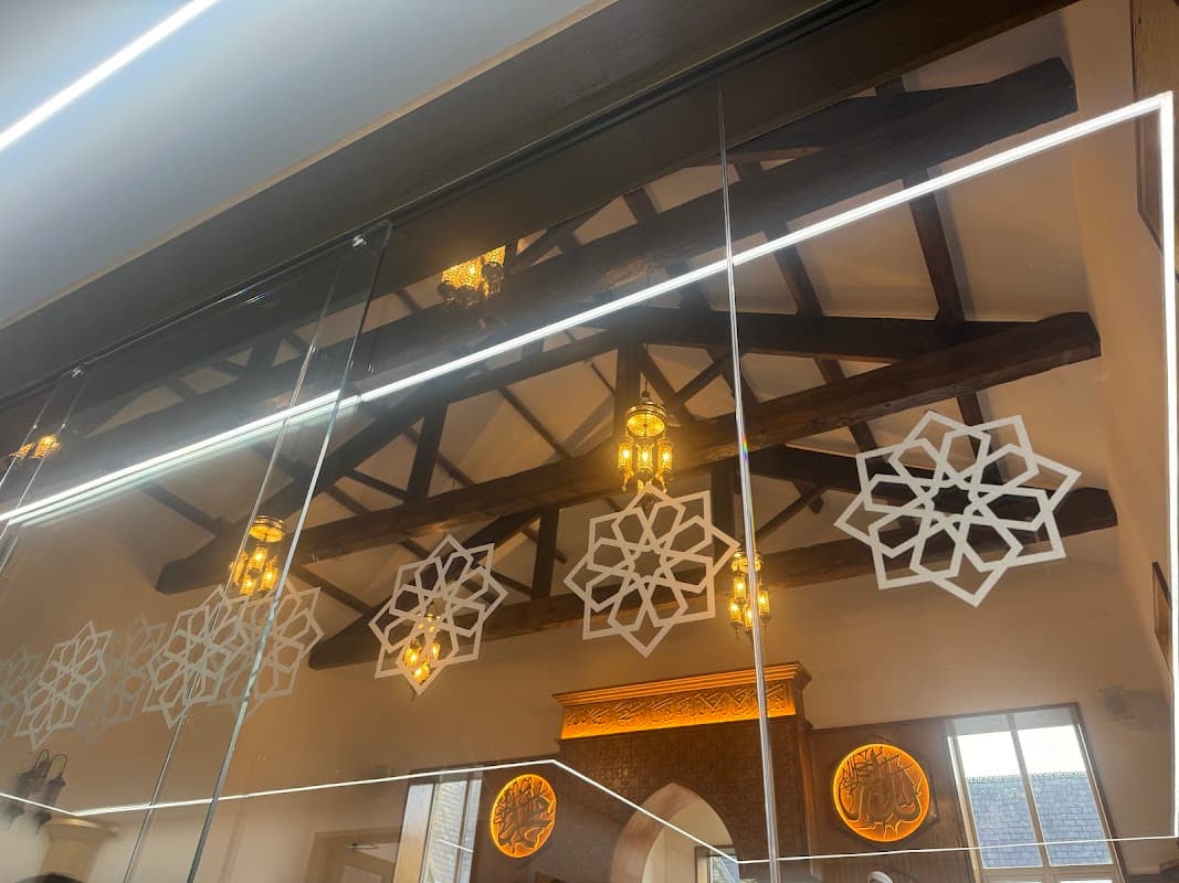 Intricate wooden beams and decorative lanterns reflect on a mirrored surface, with ornate patterns adorning the walls.