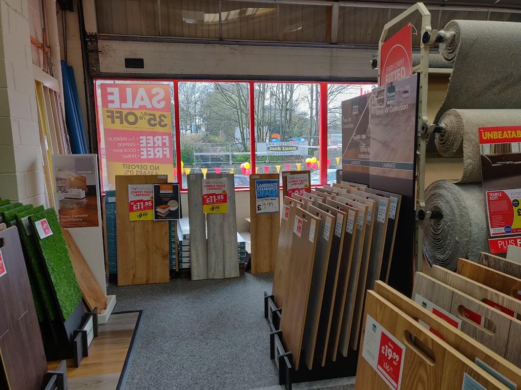Furniture shop interior showcasing flooring options, sale signs, and large windows with a view of the outdoors.