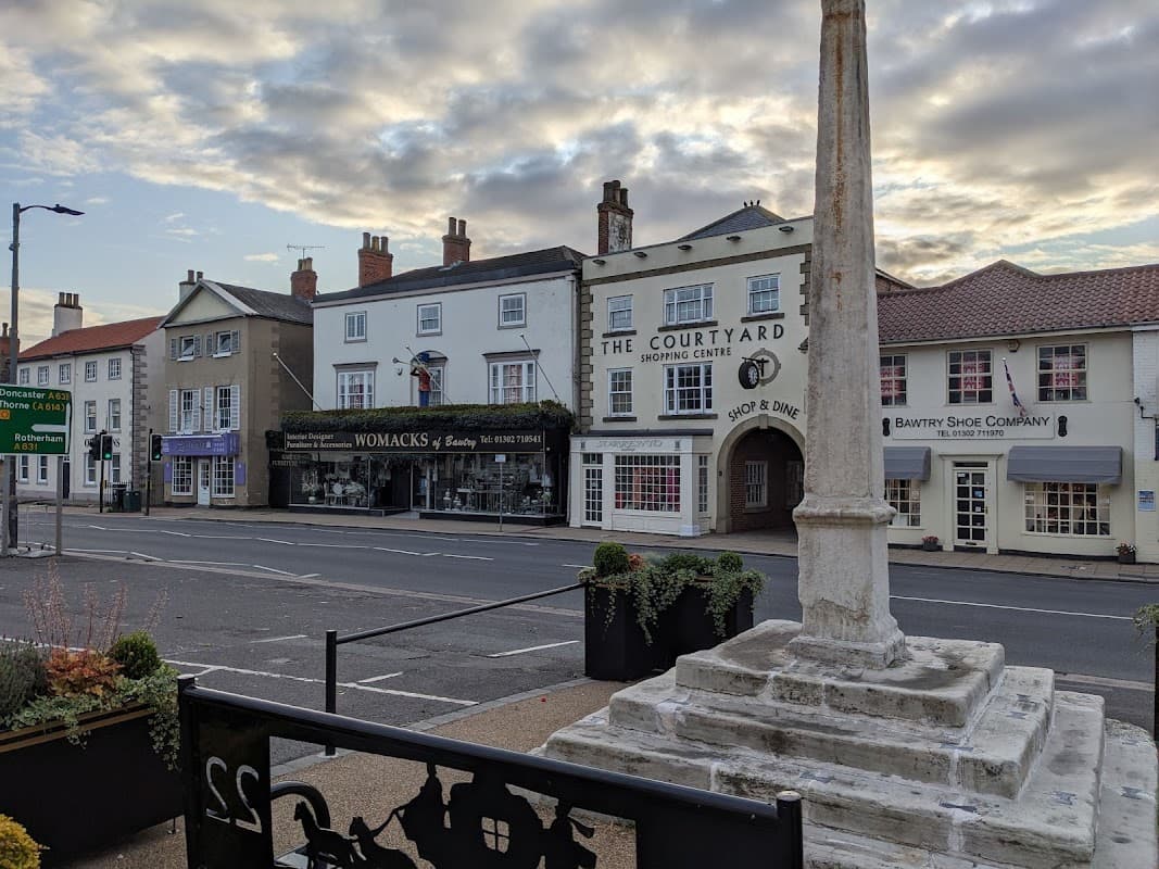 Pay & Display car park with shops, a monument, and buildings under a cloudy sky in Bawtry, Yorkshire.