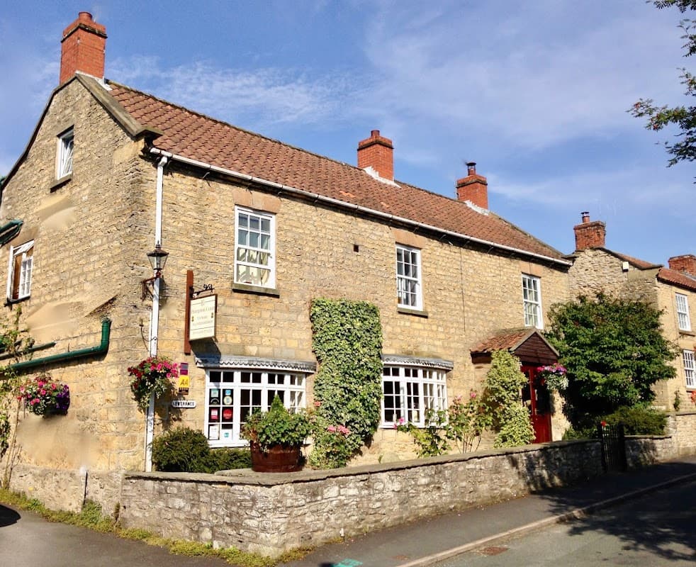 Charming stone building with a red-tiled roof, surrounded by greenery and colorful flower pots in Beadlam, Yorkshire.