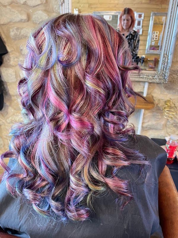Vibrant, multi-colored curly hair styled elegantly, with a reflection of a stylist in the background.