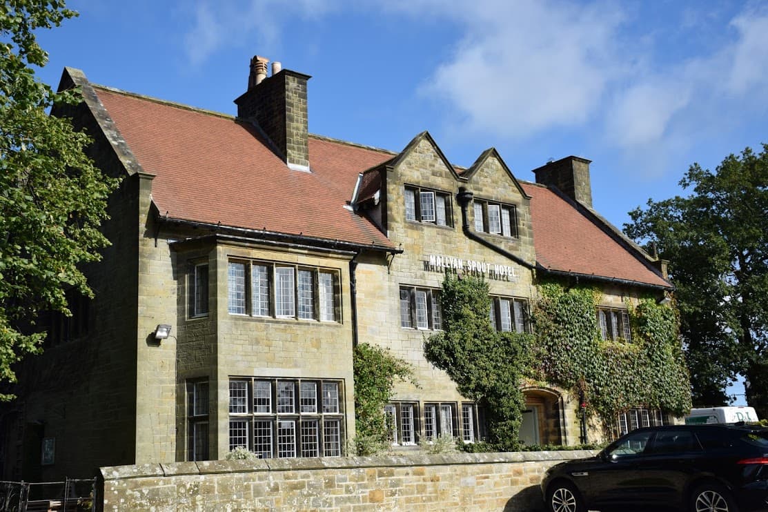 Stone building with ivy-covered walls, red roof, and large windows, set against a blue sky in Yorkshire.