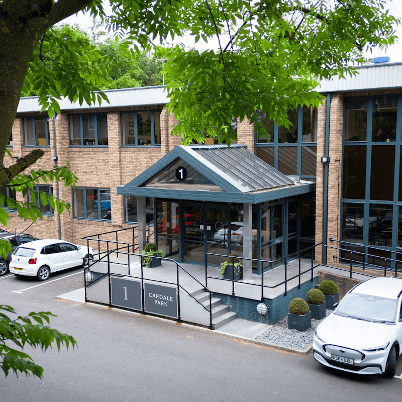 Modern brick building with a glass entrance, surrounded by greenery and parked cars, labeled "1 Cardale Park."