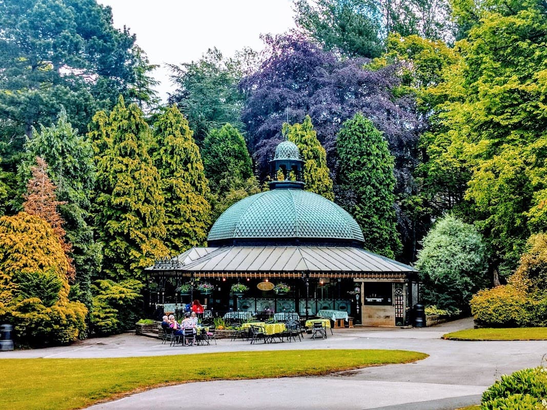 A charming octagonal pavilion surrounded by lush greenery in Valley Gardens, Harrogate, with seating and visitors.