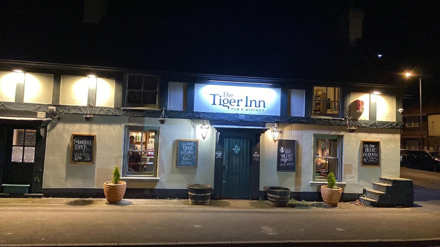 The Tiger Inn pub exterior at night, featuring illuminated signage and potted plants by the entrance.