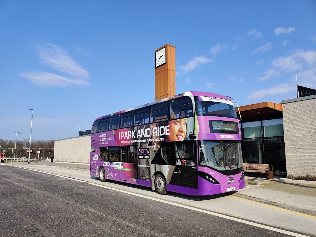 Double-decker bus at Stourton Park & Ride, modern building with a clock tower, clear blue sky in the background.
