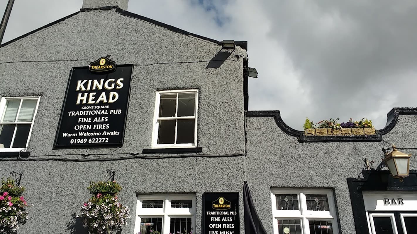 The Kings Head pub in Bellerby, Yorkshire, featuring a sign, flowers, and a welcoming atmosphere under cloudy skies.