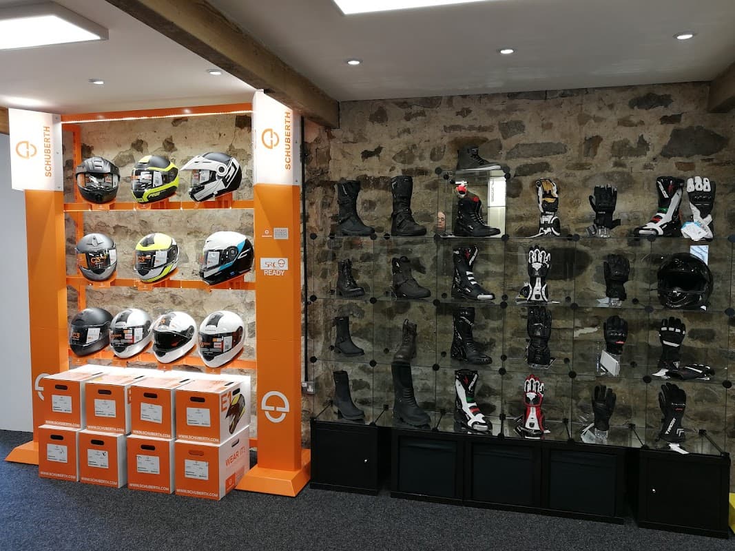 Display of motorcycle helmets and gear, including gloves and boots, in a shop with stone walls and orange accents.