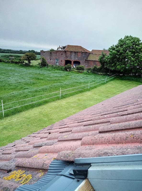 View from a roof showing a grassy field, a rustic building, and trees under a cloudy sky in Bempton, Yorkshire.