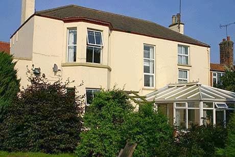 Cream-colored house with large windows, a conservatory, and surrounding greenery in Bempton, Yorkshire.