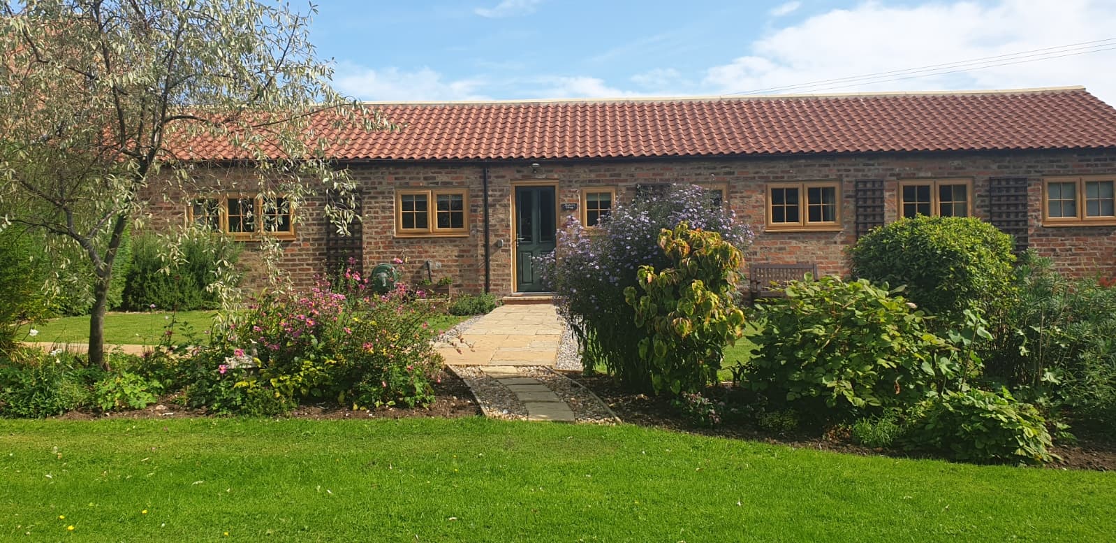 Charming brick cottage with a red tiled roof, surrounded by colorful gardens and lush greenery in Bessingby, Yorkshire.