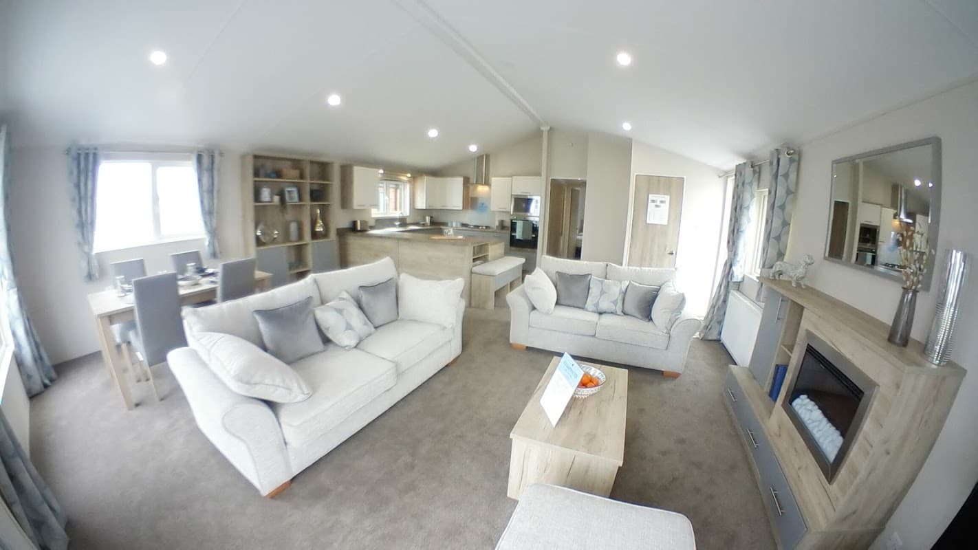 Modern lounge area with light-colored sofas, wooden furniture, and a stylish kitchen in a spacious caravan.