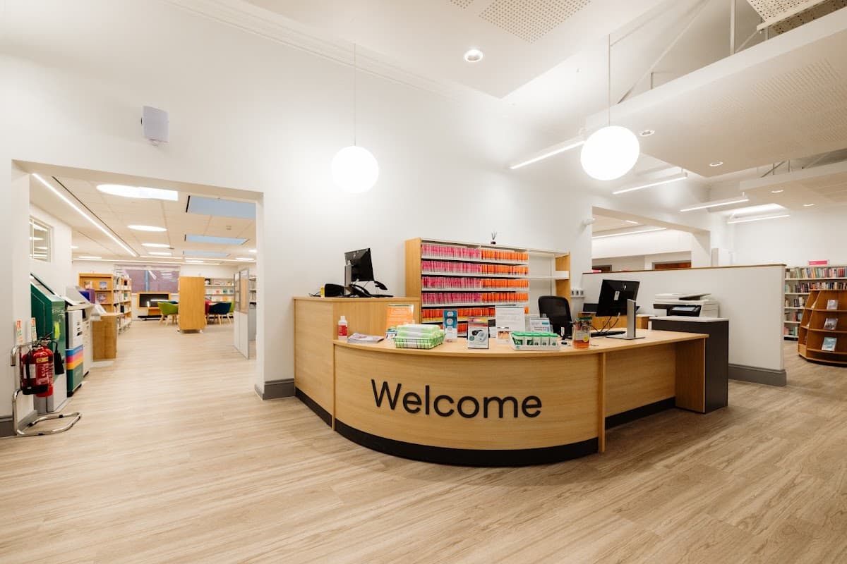 Bright, modern library interior with a welcoming reception desk and colorful book shelving in the background.