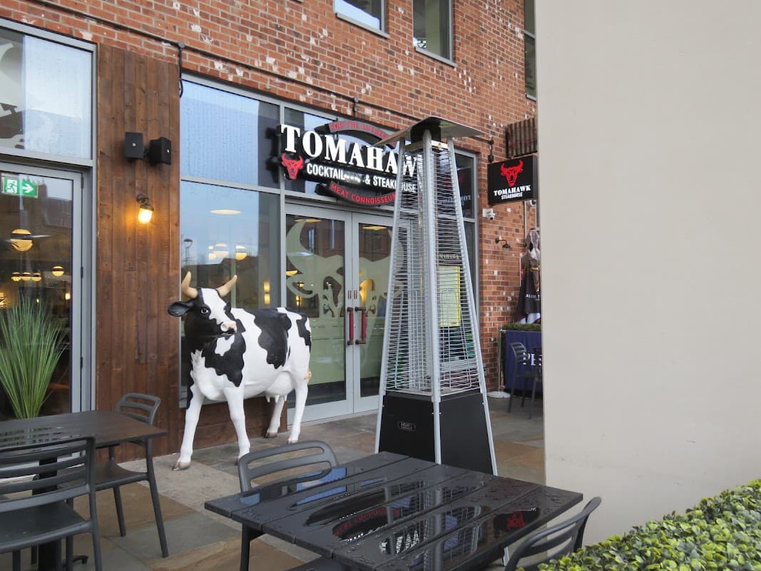 Cow statue outside Tomahawk restaurant, featuring outdoor seating and a patio heater in a brick building.