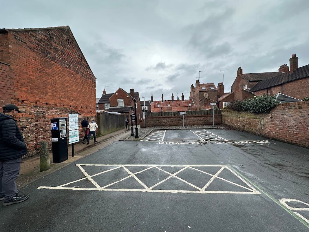 Pay & Display car park with empty disabled parking spaces, red brick buildings, and overcast sky in Beverley, Yorkshire.