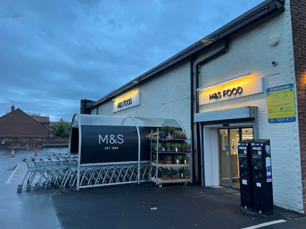 M&S Foodhall entrance with shopping carts and potted plants, under a cloudy evening sky in Beverley, Yorkshire.