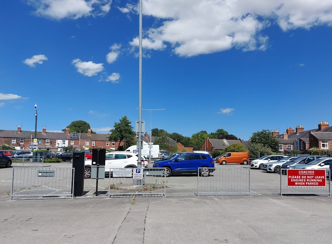 Car park with various vehicles, blue sky, and a sign instructing coaches not to park. Residential buildings in background.