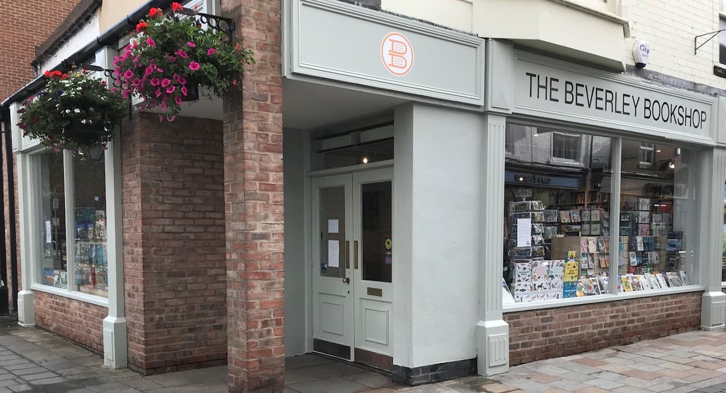 Charming brick storefront with large windows displaying books, colorful hanging flowers, and a welcoming entrance.