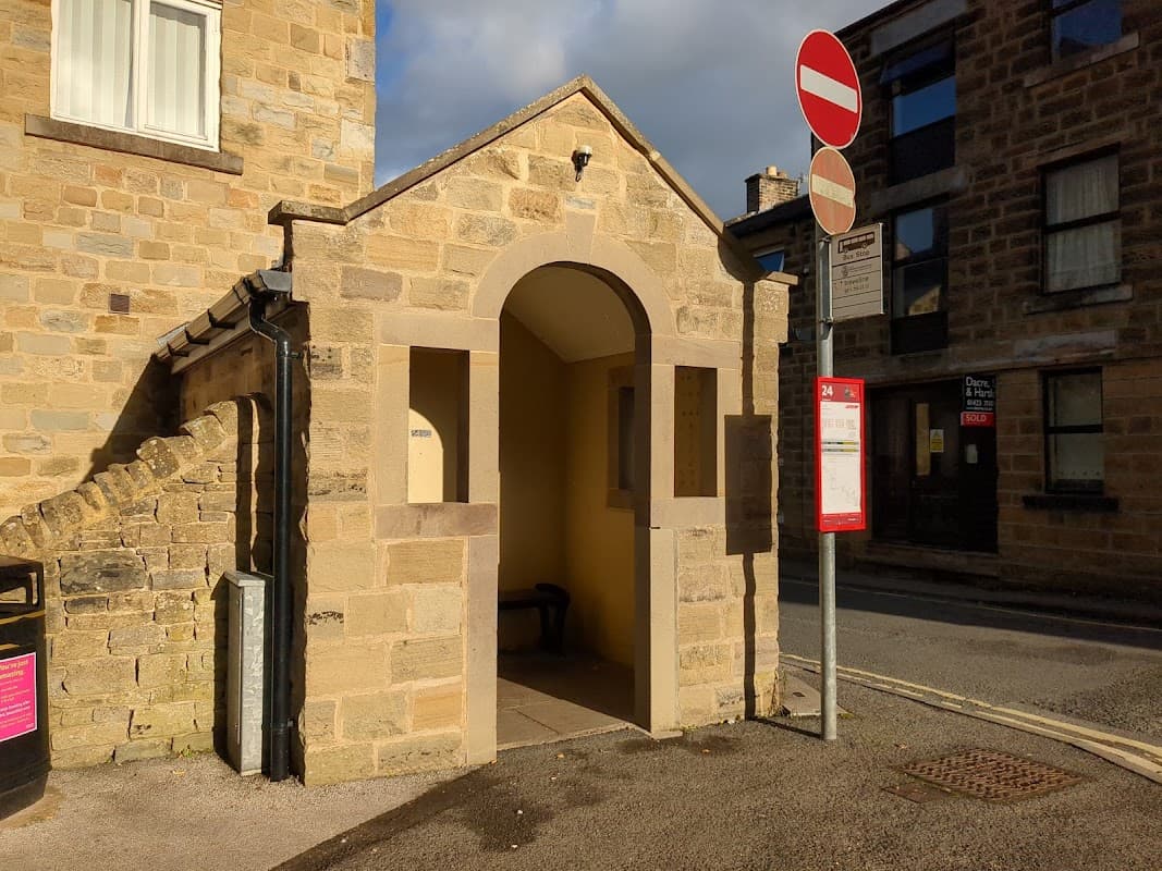 Stone archway entrance with a bench inside, near a bus stop and no entry signs on King Street, Bewerley.
