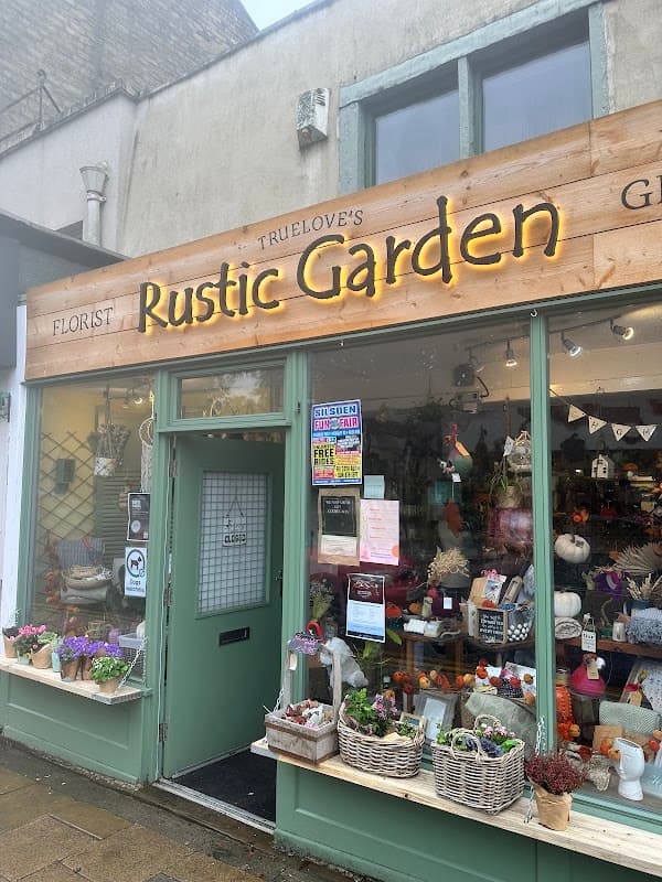 Rustic Garden florist storefront with wooden sign, colorful flowers, and decorative items in window display.